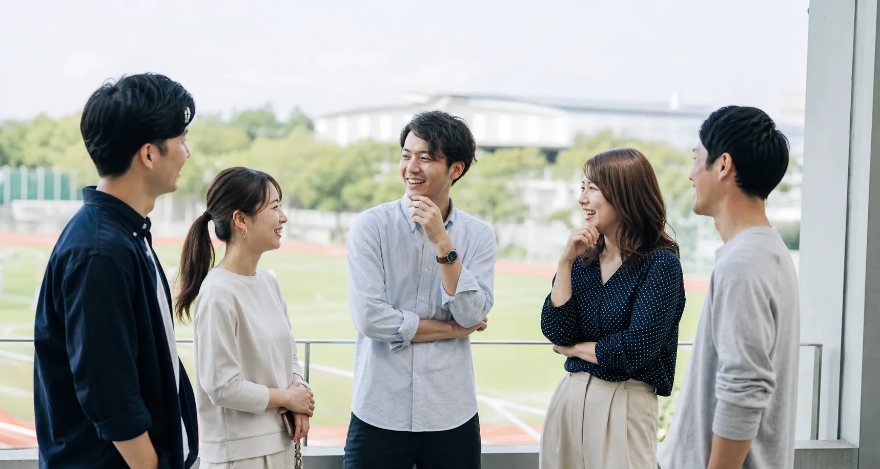 競技場を背景に談笑する若い男女のOB・OG