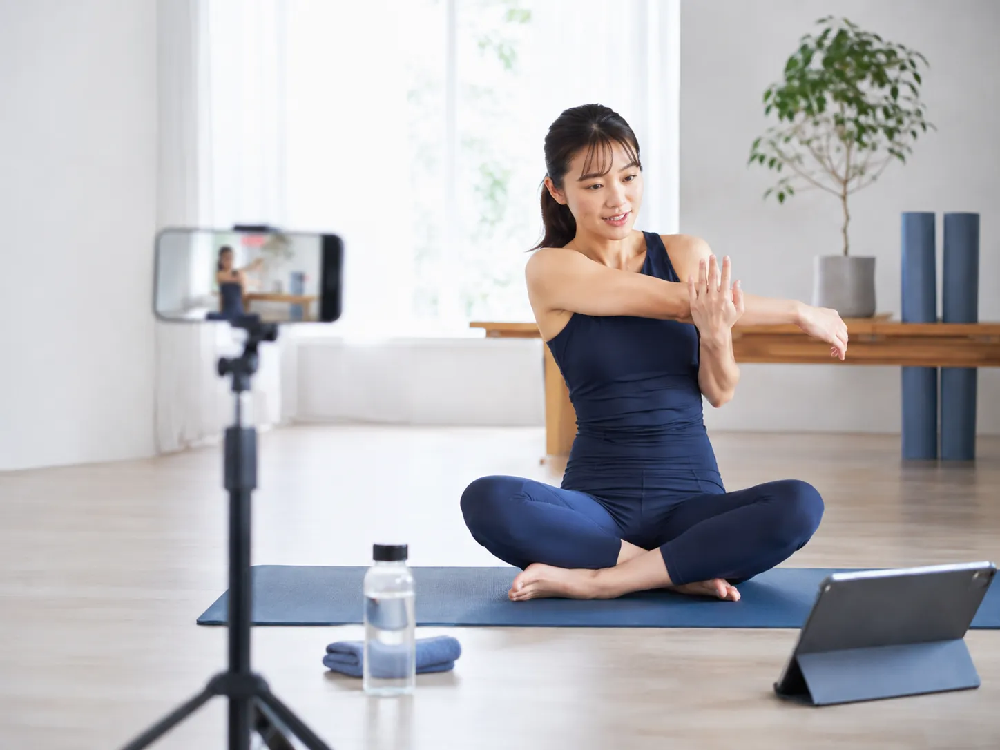 女性トレーナーがスマートフォンでオンラインレッスン動画を撮影する様子